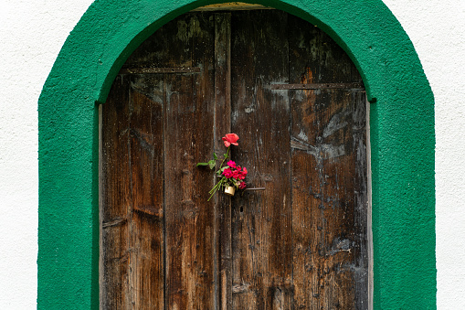 Red flowers on the doorknob on a wooden door outdoors.