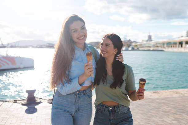 istock Two female friends having fun while eating ice cream by the sea 2149261441