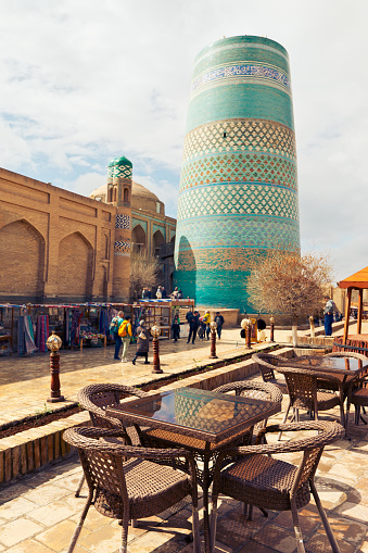 Khiva, Uzbekistan - March 26, 2024: people walk through the streets in the heart of ancient fortress Ichan Kala. View of unfinished building of Kalta Minor minaret
