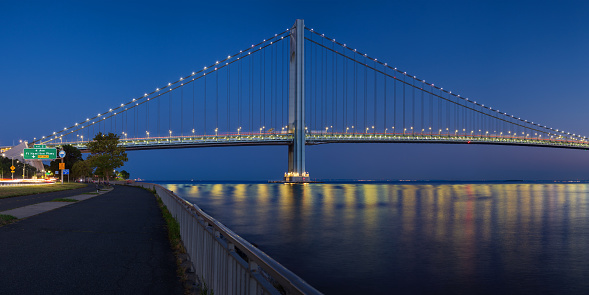 High resolution stitched panorama of the Verrazano-Narrows Bridge at Red Orange Yellow Blue Sunset. The bridge connects boroughs of Brooklyn and Staten Island in New York City. It was built in 1964 and is the largest suspension bridge in the USA. The photo was taken from the Shore promenade in Bay Ridge Brooklyn. Canon EOS 6D full frame censor camera. Canon EF 50mm F/1.8 II prime lens. 2:1 Image Aspect Ratio. This image was downsized to 50MP.