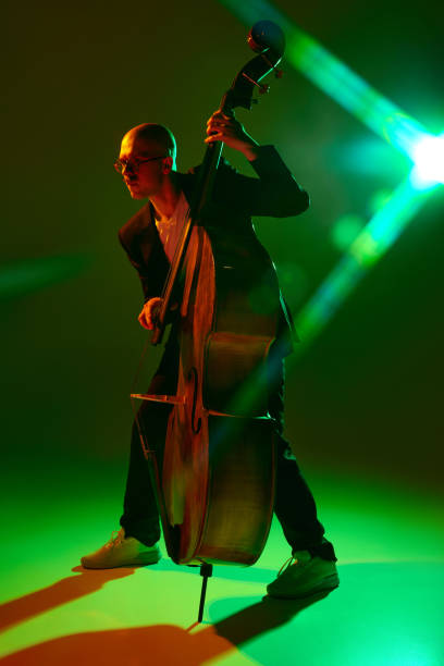 Young man dressed in a stage costume standing with glowing staff in front of  infinity mirror. Light artist is showing a colorful shapes with a spinning LED flowtoys, the shapes are reflected in the mirror. Studio shooting in dark, slow shutter speeds, long exposure, motion blur