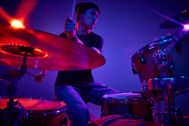 istock Drummer in casual attire practices with serious expression in pink-purple stage lighting against gradient studio background. 2149263718