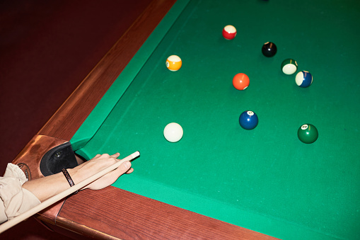 Close up of male hands holding cue stick and playing billiard at green canvas table with camera flash copy space