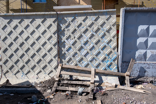 Monolithic concrete fence at a construction site with debris and broken boards on a wooden pallet on the ground