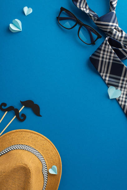 istock Creative vertical flat lay for Father's Day featuring a straw hat, stylish glasses, and checkerboard ties on a vibrant blue background 2149267180