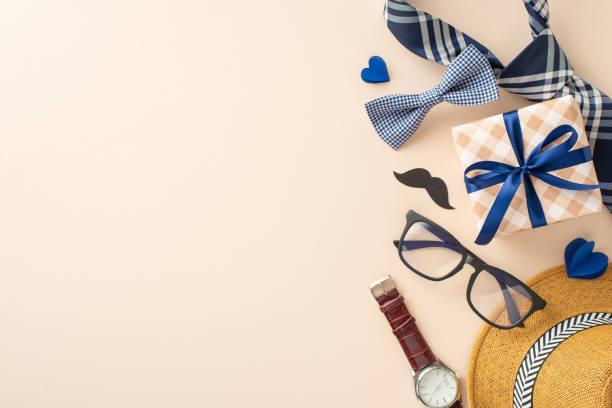 istock Festive composition for Fathers' Day with straw hat, elegant necktie, bow tie, gift box, glasses, mustache, wristwatch on pastel beige. Suitable for greetings or ads. Top view with space for message 2149267185