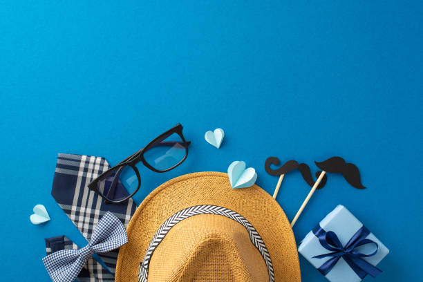 istock Creative flat lay of Father's Day gift items including a stylish straw hat, glasses, bow tie, and mustache props against a bold blue background 2149267191