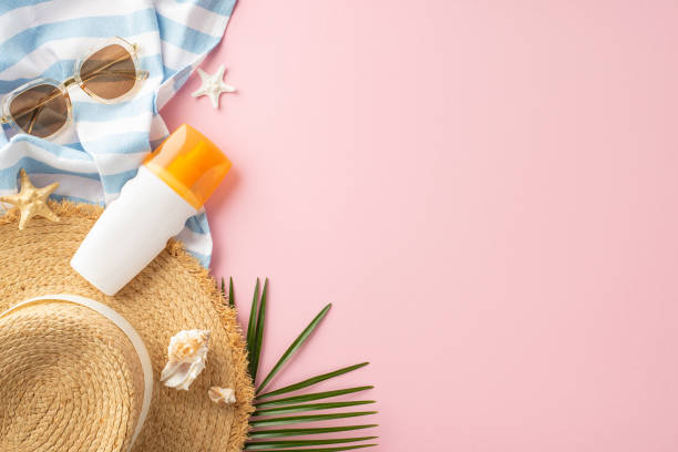 A vibrant summer holiday setup featuring sunglasses, starfish, straw hat, sunscreen, and a striped towel on a pink background. Perfect for beach and vacation-themed projects