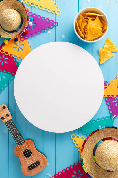 istock Colorful Cinco de Mayo display. Top-view vertical perspective showcasing festive accessories: sombreros, guitar, flag garland, nachos on rustic blue backdrop. Empty circle suitable for promotional use 2149267267