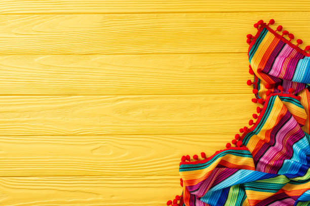 Celebrate Cinco de Mayo with this festive top view display: traditional striped serape on yellow surface. Great for themed promotions