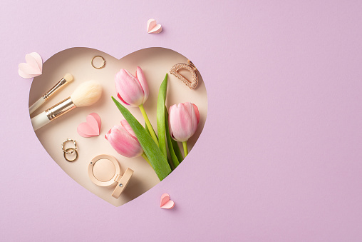 Elegant Mother's Day top view setup: Fresh tulips, makeup essentials, eyeshadow, lipstick, gold rings, barrette, paper hearts in heart-shaped frame on pastel lilac, with space for greetings or adverts