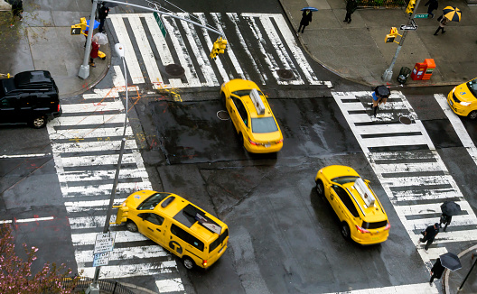 Elevated view of a yellow taxis in the centre of New York, USA.  People an be seen walking on the pavements.