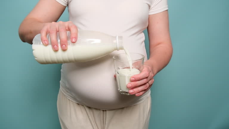 Pregnant woman holding a glass of milk in her hand, studio blue background. Concept of pregnancy and proper nutrition