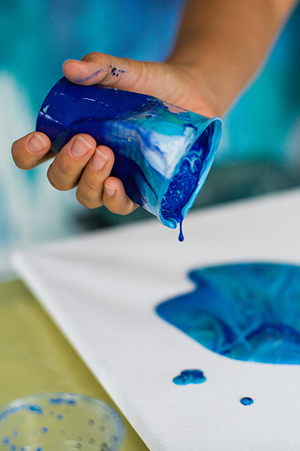 Hand pouring blue paint on a canvas