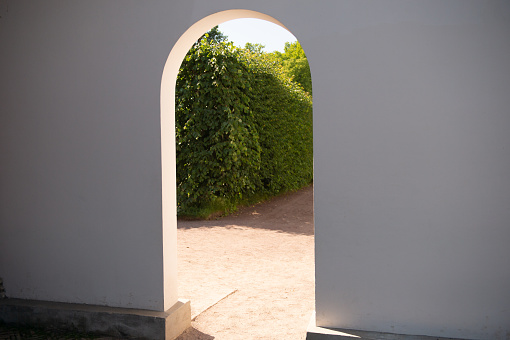 An inviting white archway opens to a pathway leading into a vibrant green garden