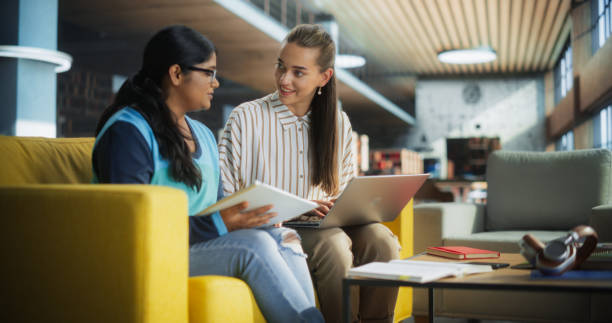 istock Two Diverse Friends and Classmates Working on a Collaborative Team Project in an Academic Library. Young Indian and Caucasian Women Using Laptop Computer for Online Learning and Virtual Lectures 2149270544