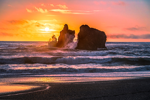 Sun setting behind waves crashing on a sea stack off of Redwoods National Park.