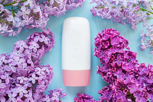 cosmetic moisturizer tube bottle with pink screw cap, lilac flowers a lot on blue background. cream, gel, skincare, shampoo, lotion, balsam, toothpaste. blank tube template mockup, bottle container