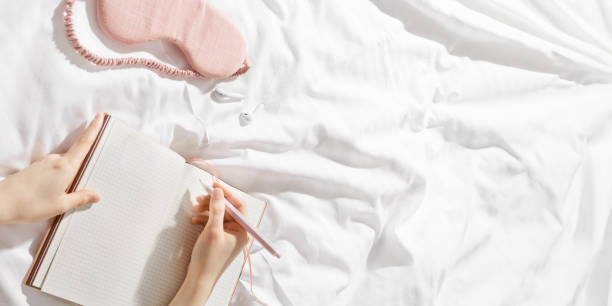 istock Woman writing on blank white page diary journal on white bedcloth in bed, holds paper notebook in hands, device free time before sleep or morning, digital detox, psychological wellbeing 2149274584