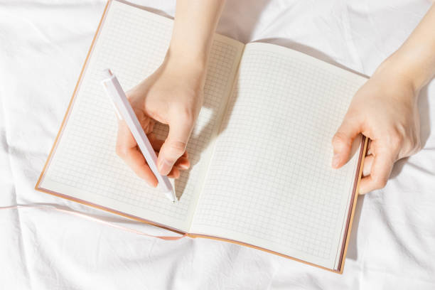 istock Woman takes notes or makes plan, day results on blank white page of paper in notebook or diary, holds notepad and pen in hands, top view, time for yourself morning or evening before sleep 2149274590