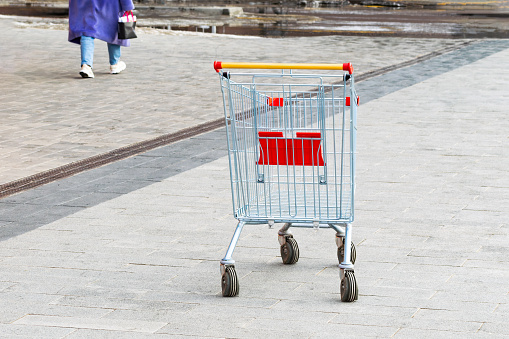 an empty shopping cart stands on the sidewalk. the concept of people lacking money for purchases. economic crisis. Shopping cart. leaving unrecognizable person. close-up