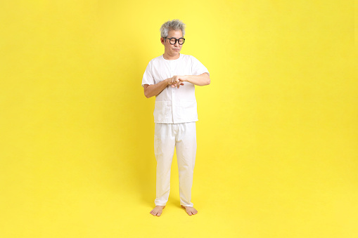 Chinese Vegetarian Festival. Senior man wearing white clothing with gesture of Waiting or late isolated on yellow background. Nine emperor god, J festival.