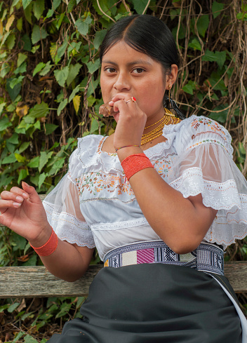 indigenous woman from Ecuador with her traditional dress eating a piece of chocolate looking shyly at the camera