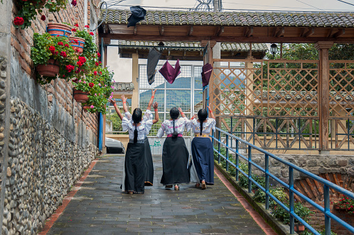 Four young Otavalo girls practice a synchronized dance routine in a charming alley with traditional architecture.