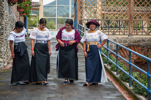 A group of indigenous women dressed in traditional costumes share a moment of joy on a picturesque bridge in the city of Otavalo, Ecuador.