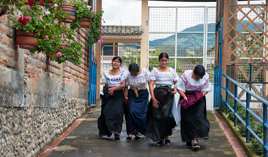 Four women in ethnic dresses share a moment of laughter as they walk along a quaint village pathway.