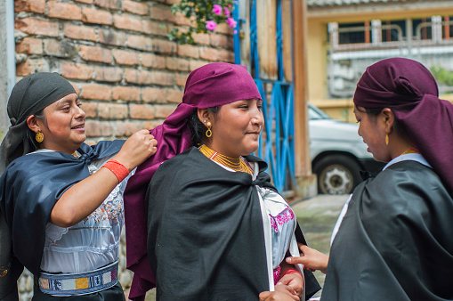 Three women engage in traditional attire adjustments during a cultural event.