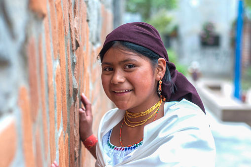 little Ecuadorian girl leaning against a wall smiling shyly at the camera
