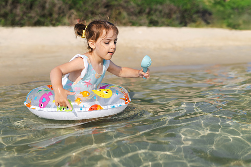 A young girl is focused on playing in shallow sea waters with a colorful floatie, holding a toy