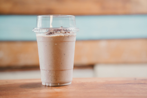 A closeup of a vanilla milkshake in a clear plastic cup with a clear lid on a wooden table.