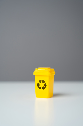 Yellow recycling bin on gray background. Selling recycled material or getting grants for green projects. Circular economy. Conserve natural resources, reduce waste, create jobs in recycling industry.