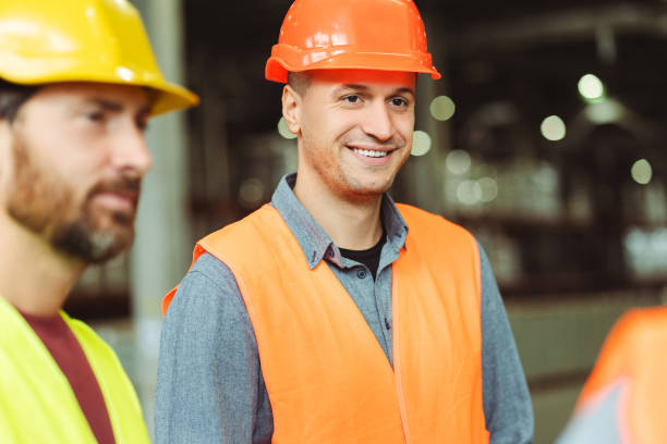 istock Attractive, man, worker, foreman wearing hard hat talking with colleagues, listening in warehouse 2149277405