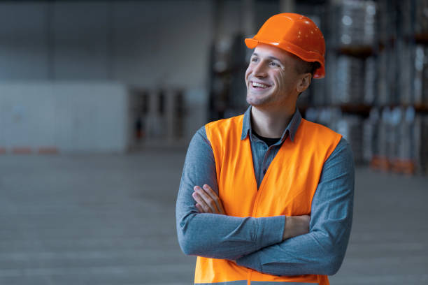 Attractive man, worker, engineer wearing workwear and hard hat, looking away with crossed arms