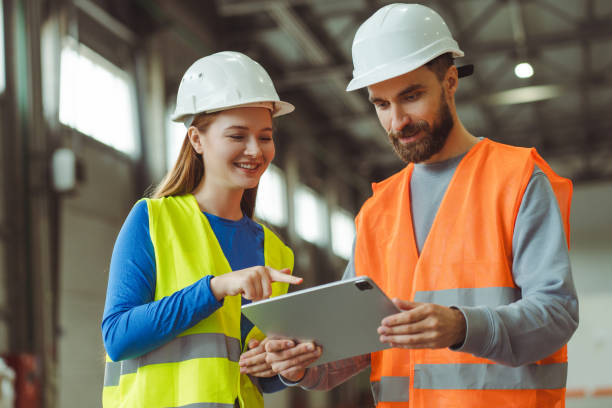 istock Engineers, factory foreman and female worker wearing protective white helmets, using digital tablet 2149277433
