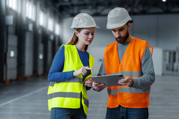 istock Attractive man and woman, engineers wearing protective workwear and hard hat using digital tablet 2149277434