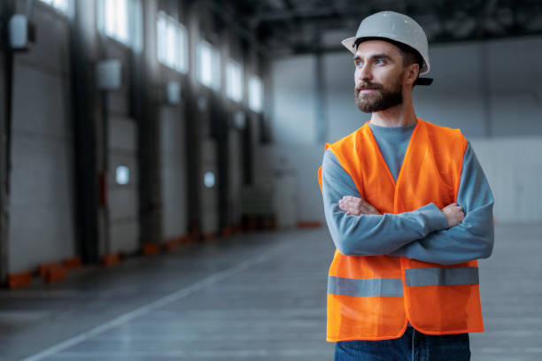 istock Smiling bearded professional engineer wearing protective workwear, white hard hat with crossed arms 2149277435