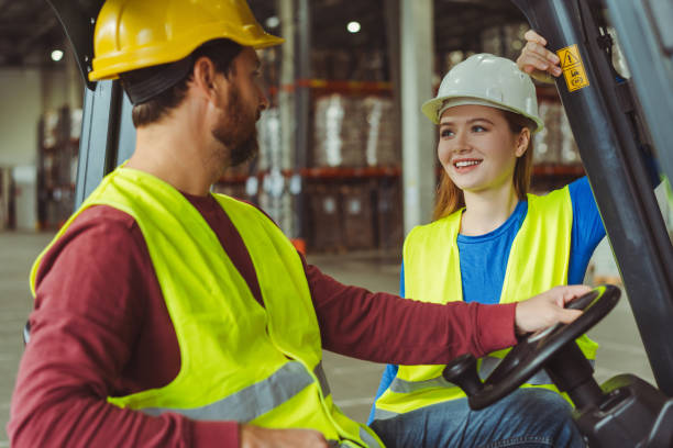 istock Positive workers wearing hard hats and workwear communicate with each other, man drives forklift 2149277466