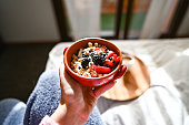 Woman holding yogurt with granola and berries in bowl.