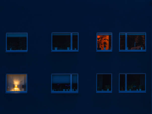 In the quiet of dusk, one window stands out brightly lit among seemingly vacant apartments in a residential building in Gothenburg, Sweden. The warm glow contrasts with the cool blue tones of the surrounding facade, hinting at life within the stillness of the evening.