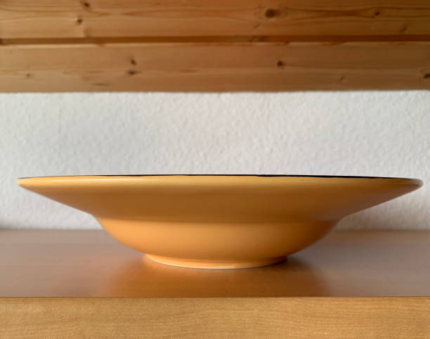 istock One deep orange plate stands on a wooden table. Side view 2149284024