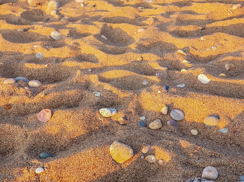 The patterns of pebbles and sand on the beach at sunset create mesmerizing natural artwork. The skys hues reflecting on the wet sand add to the beauty, making it a serene moment to behold.