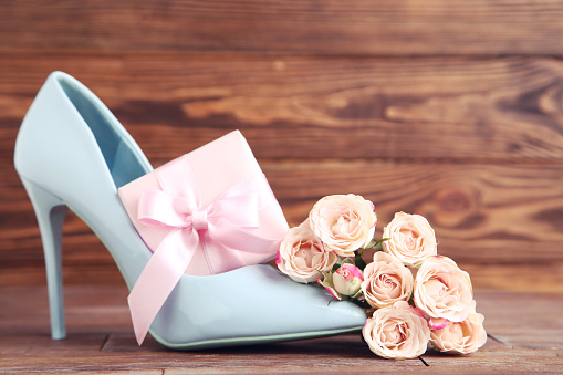 Flowers of roses, gift box and blue high-heeled shoe on brown wooden background