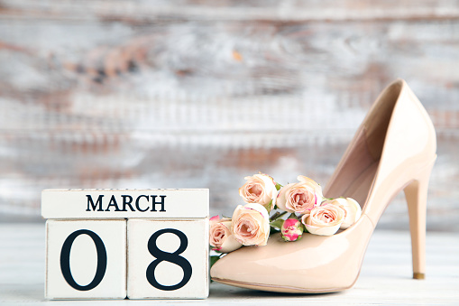 Rose flowers, cube calendar and beige high-heeled shoe on wooden background