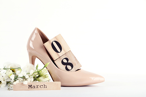Wooden calendar with high-heeled shoes and flowers on white background