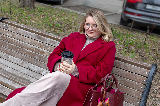 Urban Serenity: Plump woman enjoying her morning coffee on city bench. Leisure, joyful moments, Plus Size lifestyle, casual relaxation.