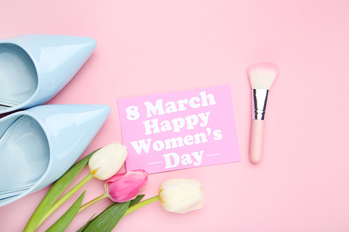 Tulip flowers and card with text 8 march Happy Womens Day, blue high heeled shoes and makeup brush on pink background